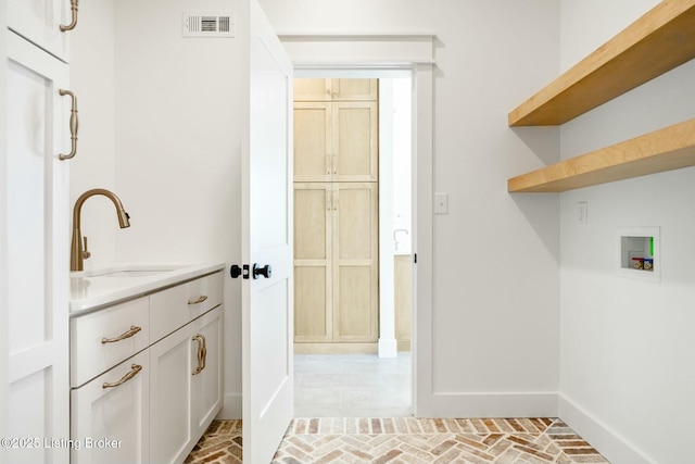 laundry area with visible vents, baseboards, washer hookup, brick floor, and a sink