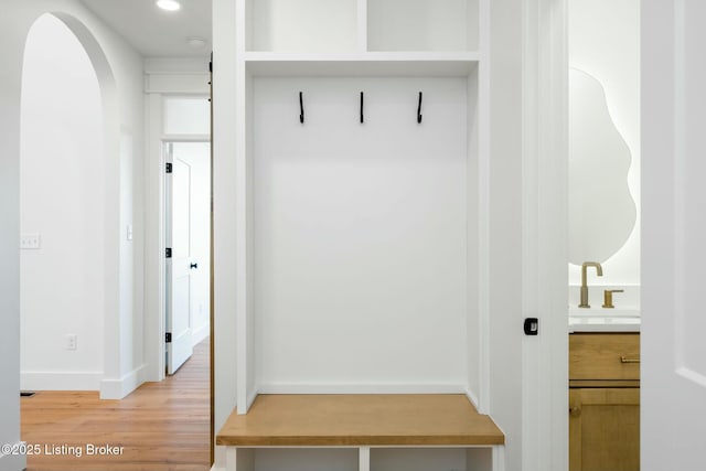 mudroom with baseboards, recessed lighting, light wood-style flooring, arched walkways, and a sink