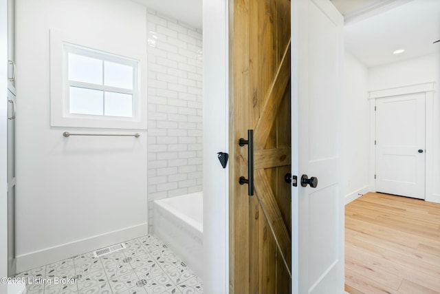 bathroom with a washtub, a shower, baseboards, and wood finished floors