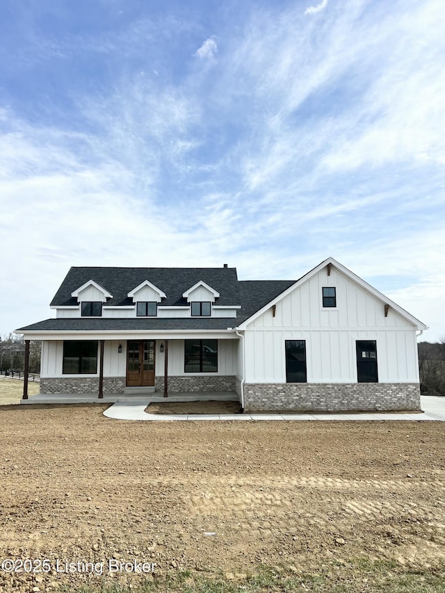 modern inspired farmhouse with a shingled roof, covered porch, french doors, board and batten siding, and brick siding