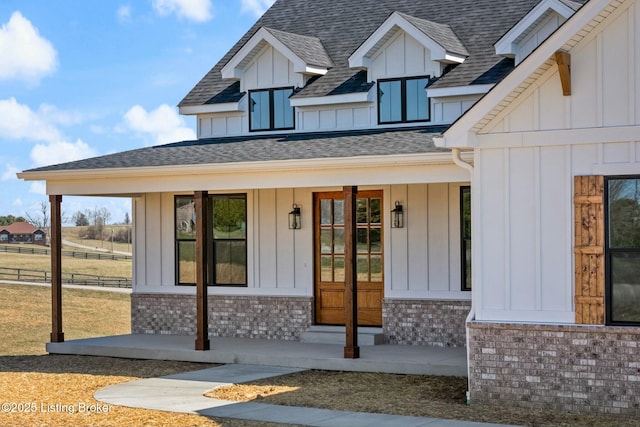 doorway to property featuring a porch, roof with shingles, board and batten siding, and brick siding