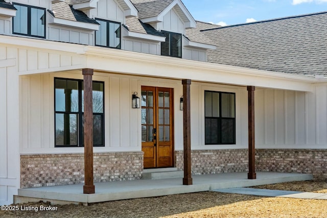 view of exterior entry with board and batten siding, brick siding, and roof with shingles