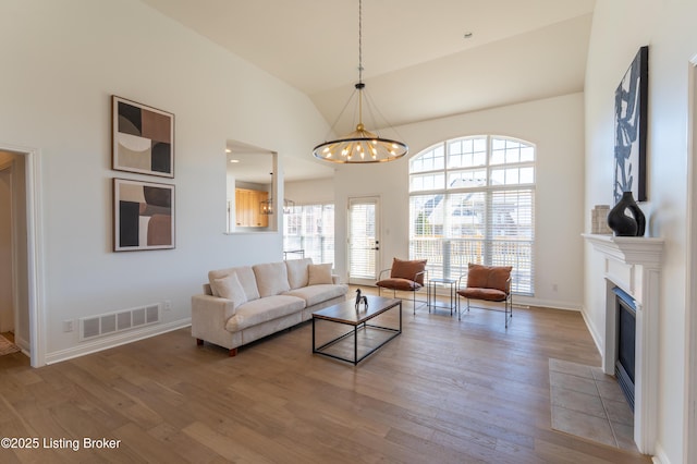 living area featuring high vaulted ceiling, light wood-style floors, visible vents, and a notable chandelier