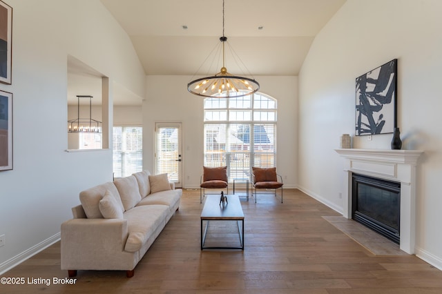 living room featuring vaulted ceiling, a fireplace with flush hearth, wood finished floors, and an inviting chandelier