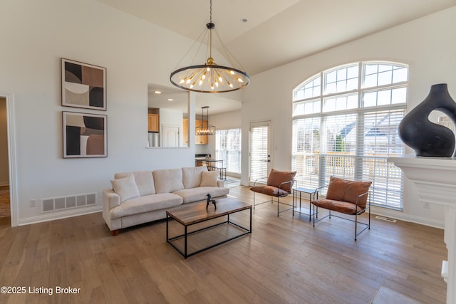 living room with a high ceiling, wood finished floors, visible vents, and a notable chandelier