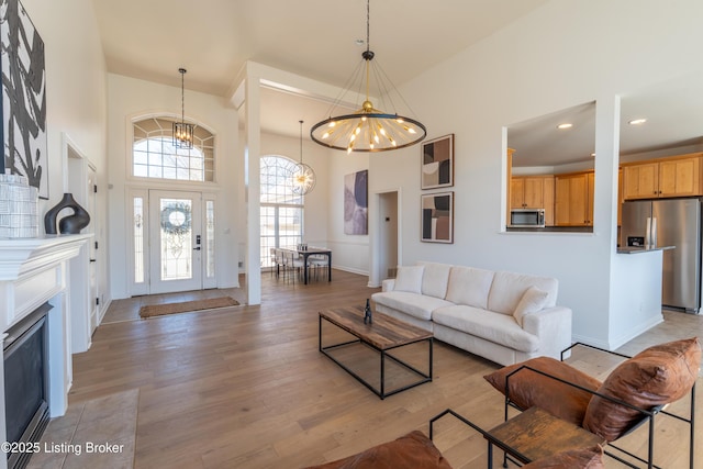 living room featuring light wood-style floors, recessed lighting, a notable chandelier, and a high ceiling