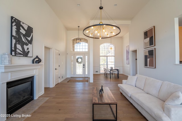 living room with a towering ceiling, an inviting chandelier, a fireplace with flush hearth, wood finished floors, and baseboards