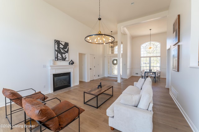 living room with visible vents, a fireplace with flush hearth, a high ceiling, light wood-type flooring, and a notable chandelier