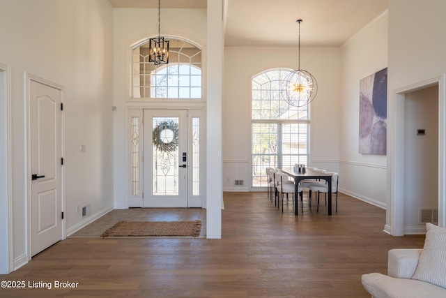 entryway with plenty of natural light, visible vents, a towering ceiling, wood finished floors, and a chandelier