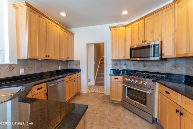 kitchen featuring appliances with stainless steel finishes, backsplash, dark stone countertops, and light tile patterned floors