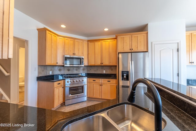 kitchen with backsplash, dark stone counters, stainless steel appliances, and a sink