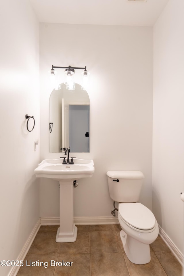 half bath with toilet, baseboards, a sink, and tile patterned floors