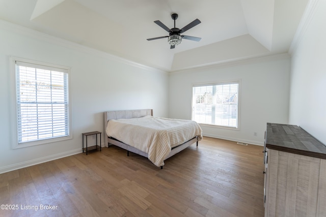 unfurnished bedroom with crown molding, multiple windows, a raised ceiling, and wood finished floors