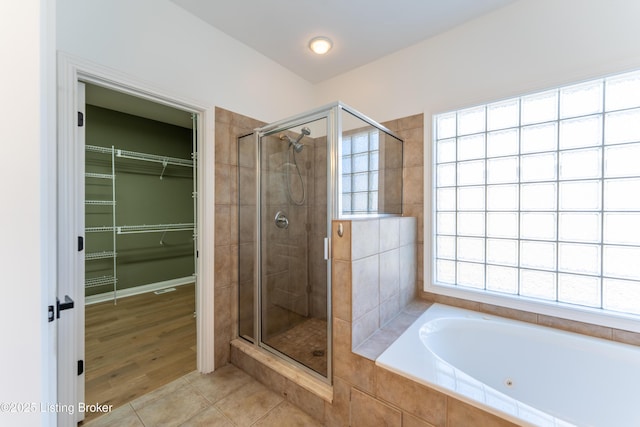 bathroom with a stall shower, a walk in closet, a garden tub, and tile patterned floors