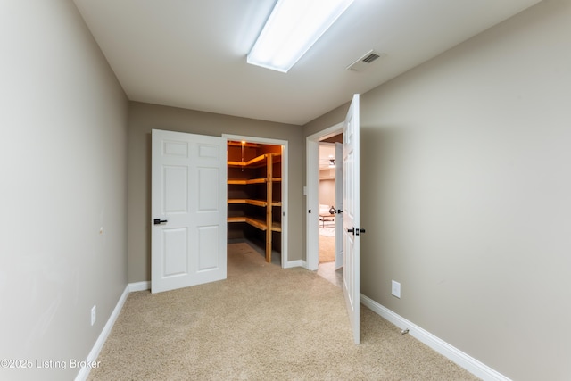 unfurnished bedroom featuring visible vents, light carpet, a spacious closet, and baseboards