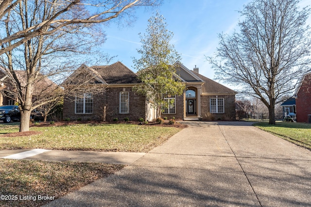 view of front of house with concrete driveway, a front lawn, a chimney, and brick siding