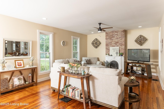 living area featuring baseboards, recessed lighting, ceiling fan, wood-type flooring, and a large fireplace