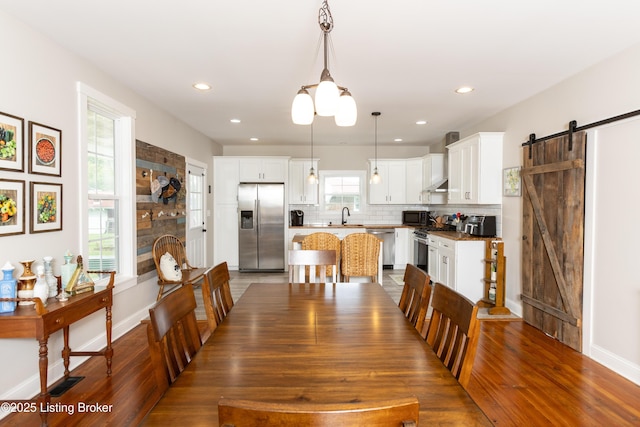 dining space with baseboards, a barn door, a stone fireplace, recessed lighting, and wood finished floors