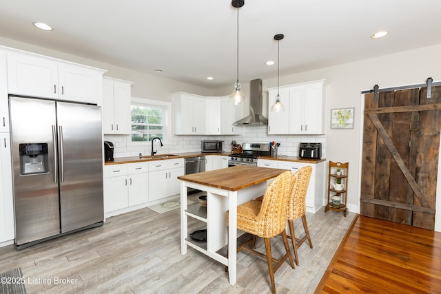 kitchen featuring a sink, stainless steel appliances, a barn door, wall chimney exhaust hood, and wooden counters