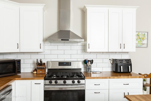 kitchen featuring backsplash, stainless steel appliances, white cabinets, butcher block counters, and wall chimney range hood