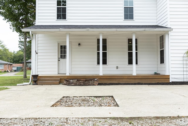 property entrance featuring covered porch and a shingled roof