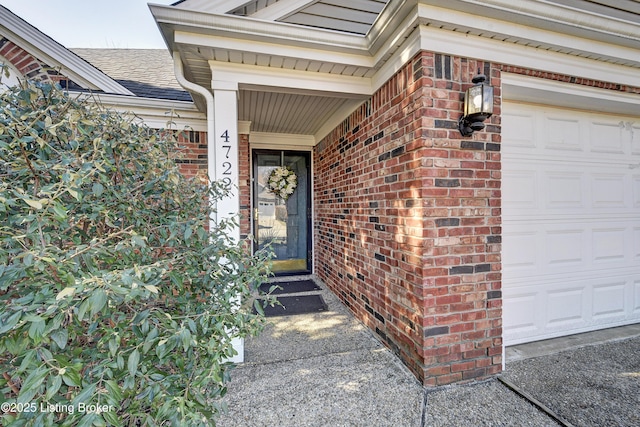 view of exterior entry featuring an attached garage, a shingled roof, and brick siding