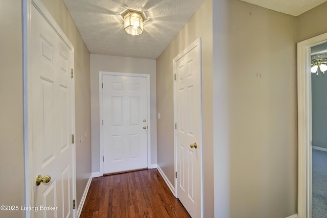 hall featuring a textured ceiling, dark wood-type flooring, and baseboards