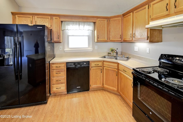 kitchen featuring light countertops, light wood-style floors, a sink, under cabinet range hood, and black appliances