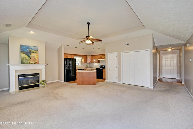 kitchen featuring light carpet, a fireplace with flush hearth, a kitchen island, open floor plan, and black appliances