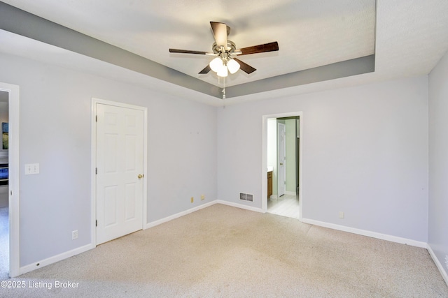 unfurnished room with visible vents, baseboards, a ceiling fan, a raised ceiling, and carpet flooring