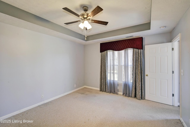 carpeted empty room with baseboards, a raised ceiling, and a ceiling fan