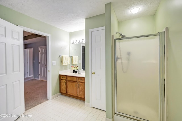 bathroom featuring a stall shower, vanity, a textured ceiling, baseboards, and tile patterned floors