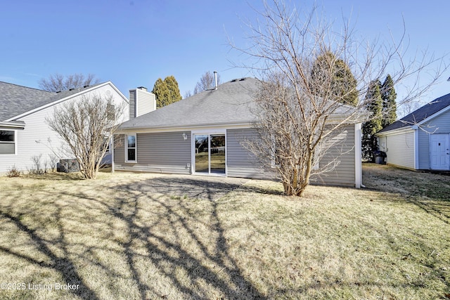 rear view of house with a yard, a shingled roof, a chimney, and an outdoor structure