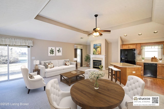 living area featuring a glass covered fireplace, lofted ceiling, a tray ceiling, and recessed lighting