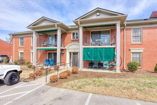 view of front of home featuring a balcony, uncovered parking, and brick siding