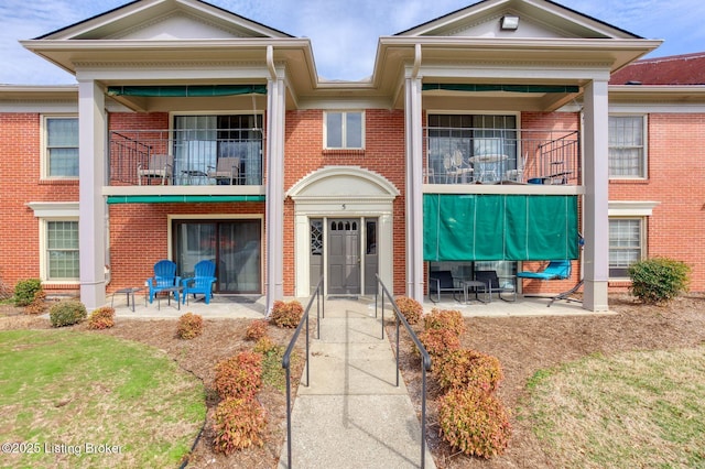 view of front of property featuring a patio area, brick siding, and a balcony