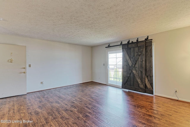 unfurnished room featuring a barn door, a textured ceiling, baseboards, and wood finished floors