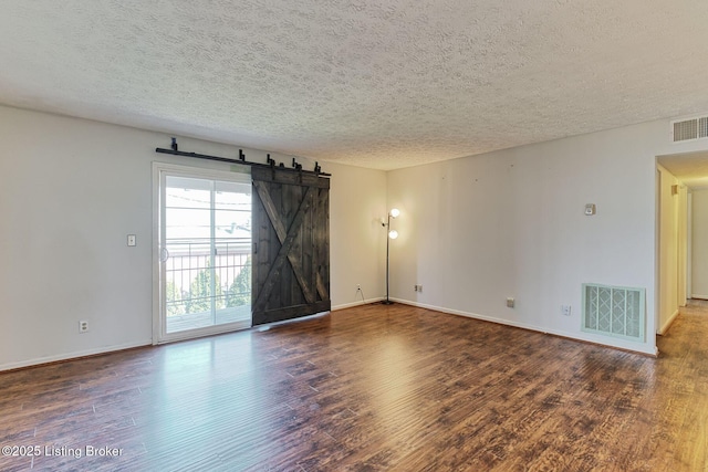 empty room featuring wood finished floors, visible vents, a textured ceiling, and a barn door