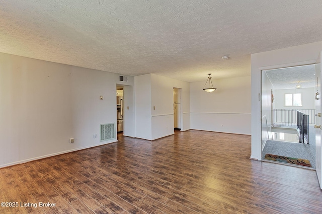 empty room featuring baseboards, a textured ceiling, visible vents, and dark wood-type flooring