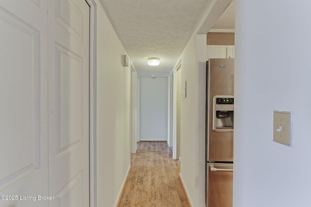 hall featuring light wood-type flooring, a textured ceiling, and baseboards