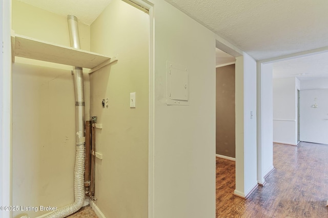 hallway featuring electric panel, a textured ceiling, baseboards, and wood finished floors