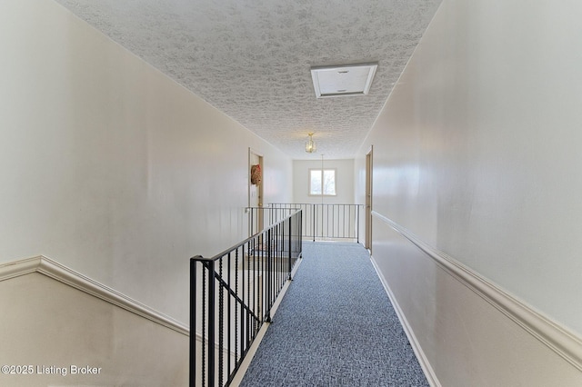 hallway with a textured ceiling, carpet flooring, and an upstairs landing