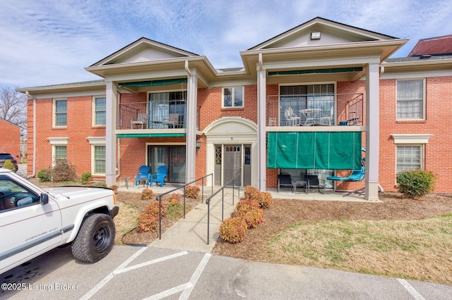 view of front of home with a balcony, uncovered parking, and brick siding