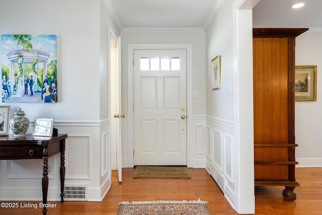 foyer featuring crown molding, light wood finished floors, visible vents, a decorative wall, and wainscoting