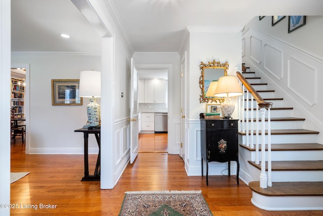 entrance foyer with ornamental molding, stairway, and light wood finished floors