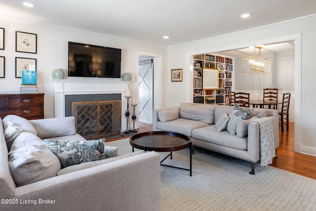 living area with a notable chandelier, ornamental molding, wood finished floors, and a fireplace with flush hearth