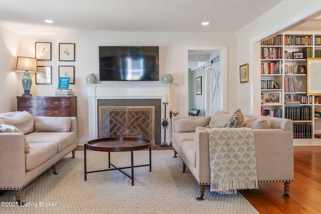 living area featuring a barn door, a fireplace with flush hearth, wood finished floors, built in features, and crown molding