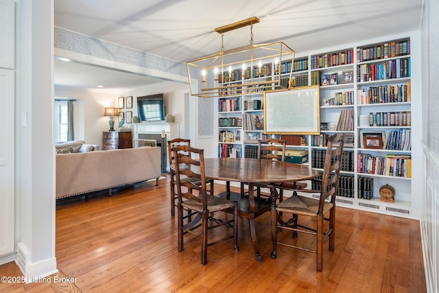 dining space featuring a chandelier, a fireplace, built in shelves, and wood finished floors