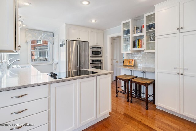 kitchen with a sink, white cabinetry, appliances with stainless steel finishes, backsplash, and glass insert cabinets