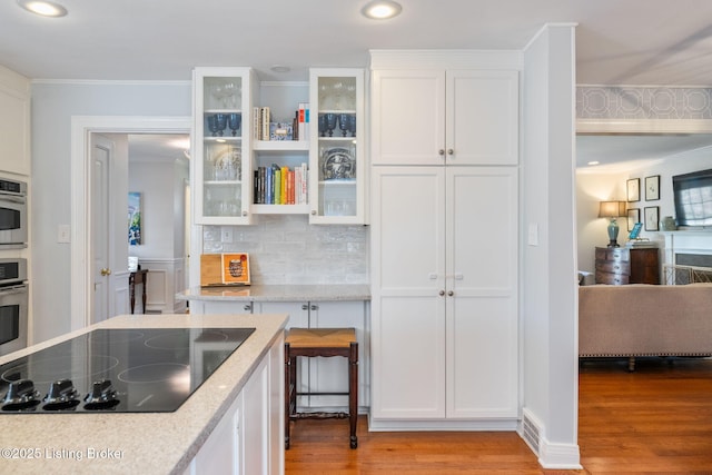 kitchen featuring stainless steel oven, black electric stovetop, light wood-type flooring, white cabinetry, and backsplash